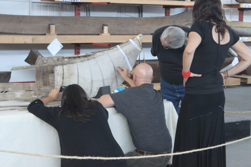 Four people gather around a bow of a canoe for repair