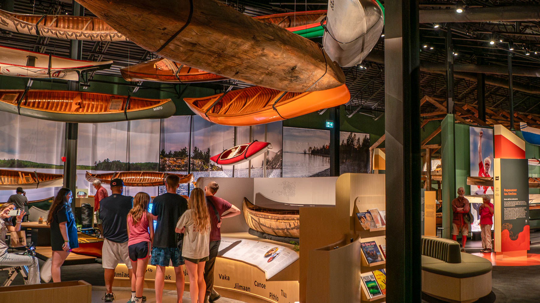 A family stands in the Headwaters exhibit in The Canadian Canoe Museum's Exhibition Hall. Canoes hang overhead.