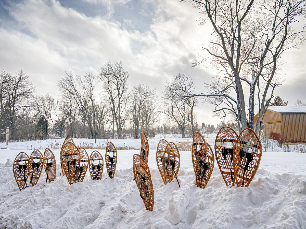 Snow shoes stand in a snow bank on the Lakefront Campus, with the lake and Canoe House in the background.