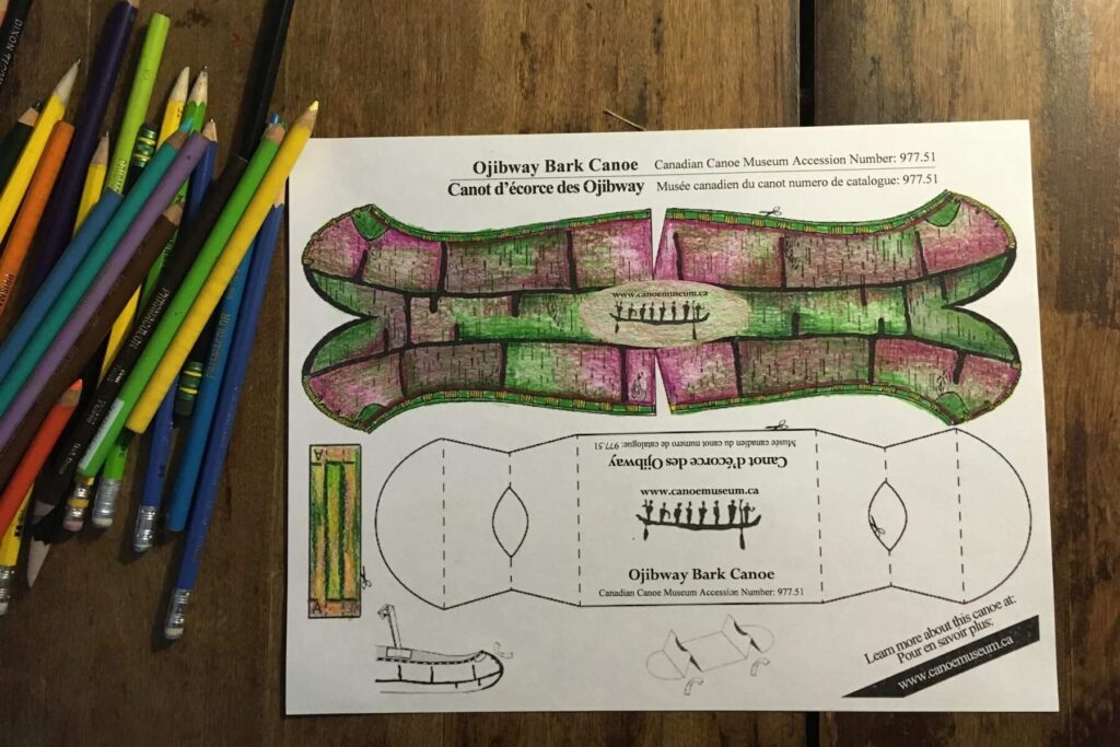 Colorful pencil crayons lay beside a canoe cutout printable, filled in with green and pink