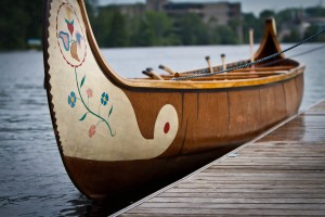 A birch canoe with painted floral designs on the bow floats next to a dock.