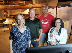 Four people pose for a picture in front of birchbark canoe display