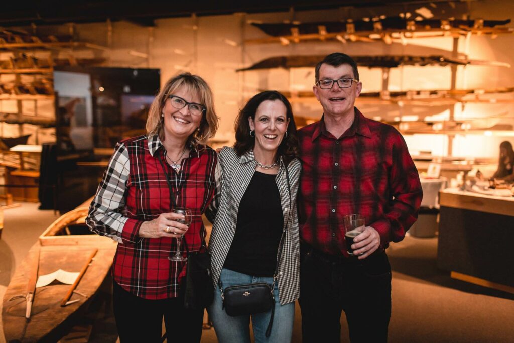 Three attendees of a Campfires & Cocktails event smile toward the camera while holding cocktails.