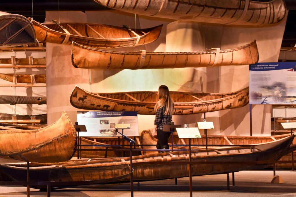 A visitor admires a display of several birch canoes hanging on a wall.