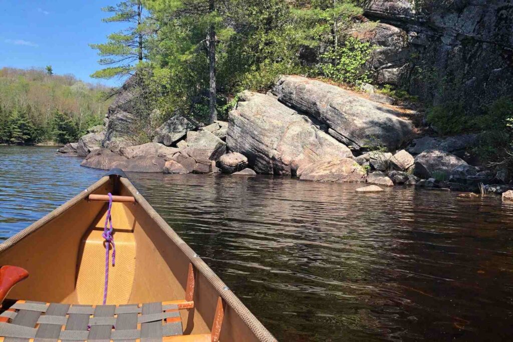 Bow of a canoe in calm water pointed toward Canadian Shield rocks