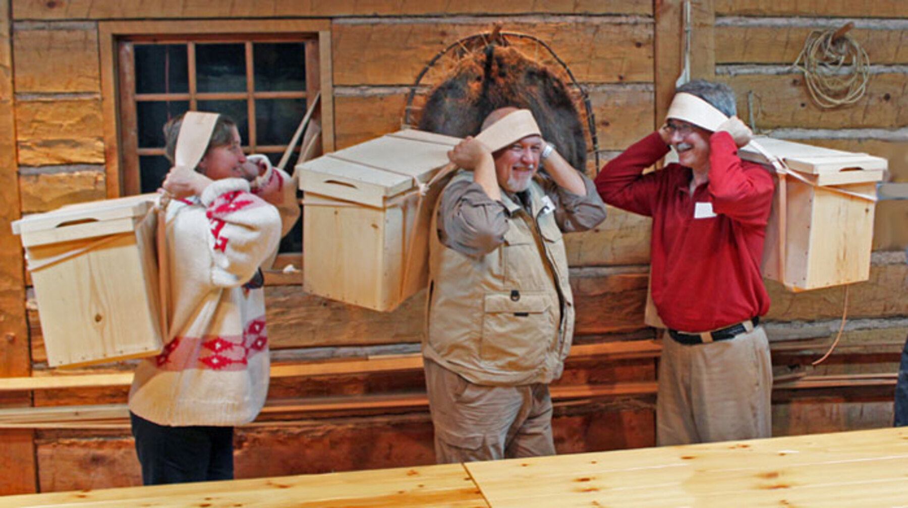 Three people carry a Wanigan on their backs using the strap that sits across their foreheads.