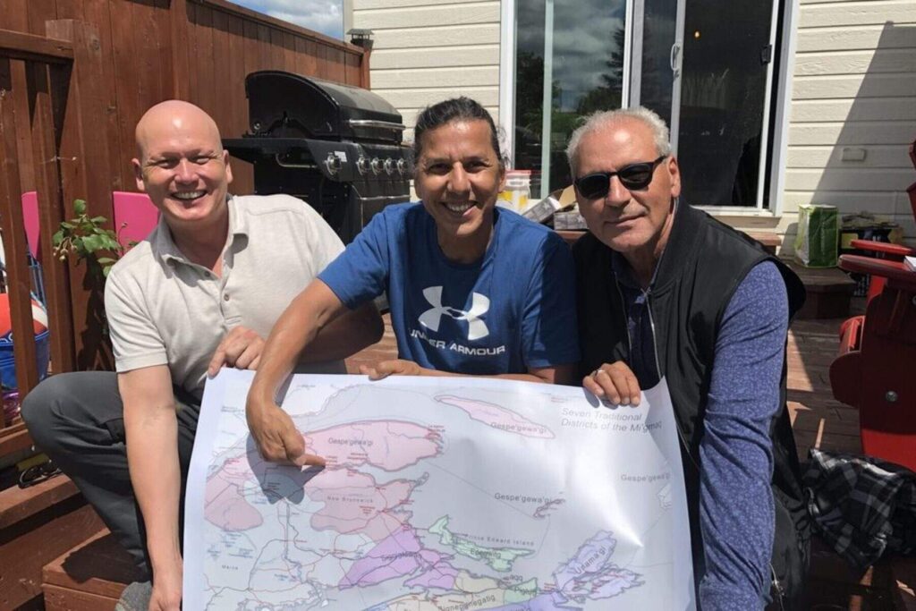 Robin Cavanagh, Jeremy Ward, and Fred Metallic pose while holding a traditional map of the districts of the Mi'gmaq