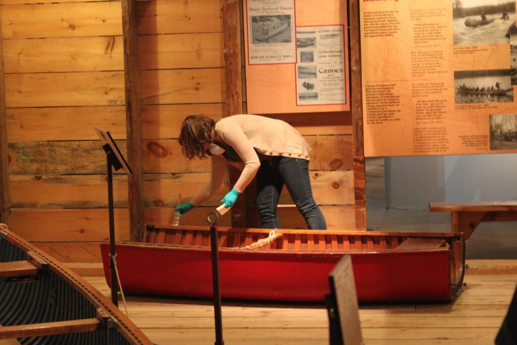 Someone uses a brush to clean the gunwales of a canoe on display.