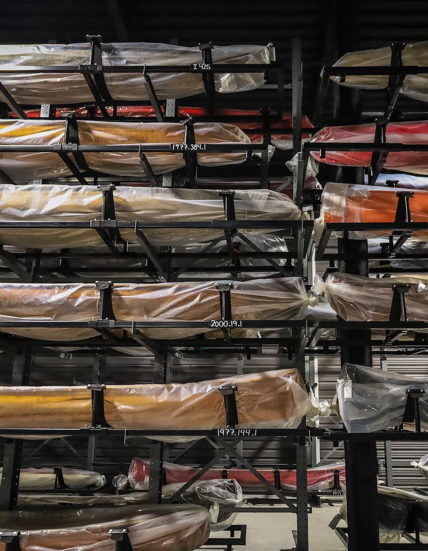 Canoes temporarily wrapped in protective plastic and of various sizes and colours line the racks of the Collection Hall in the Canadian Canoe Museum.