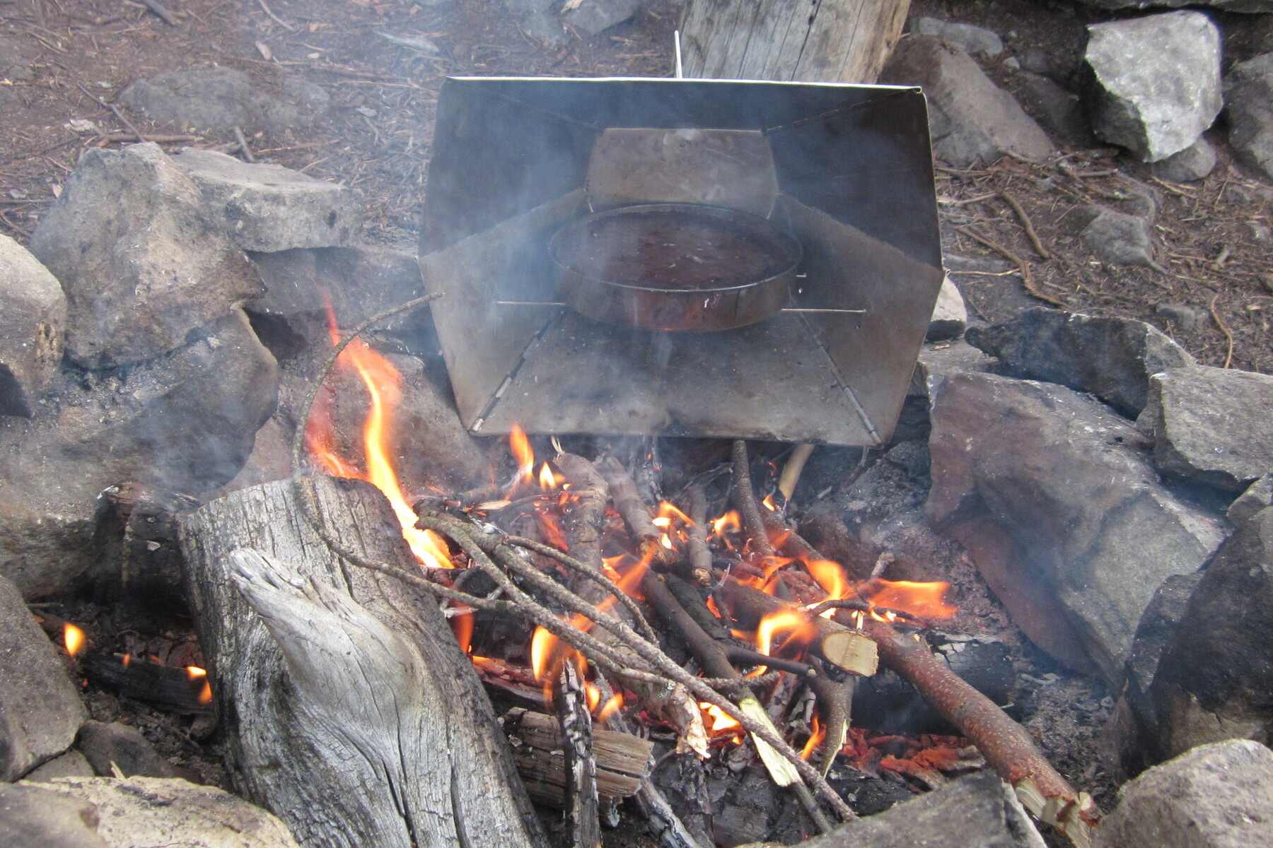 Cooking equipment rests on top of stones with campfire underneath