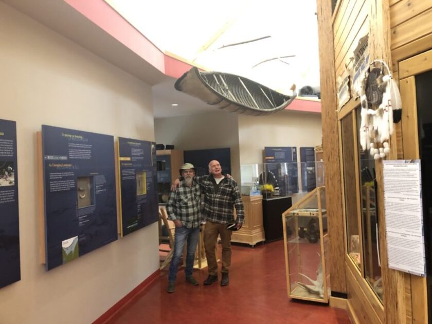 Two men standing in a hallway with displays and a canoe hanging from ceiling above