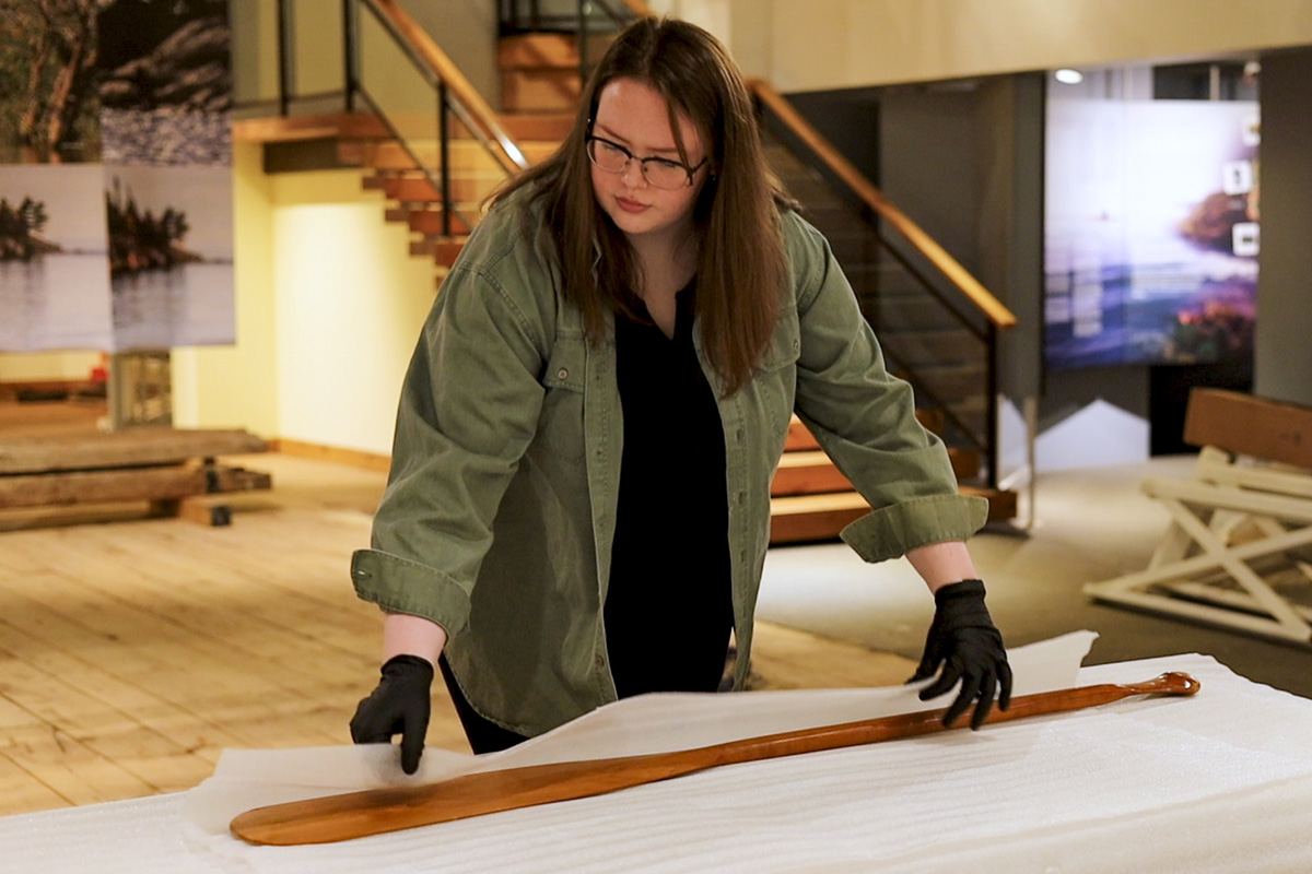 A curatorial intern wraps a paddle in packing foam for safe transport.