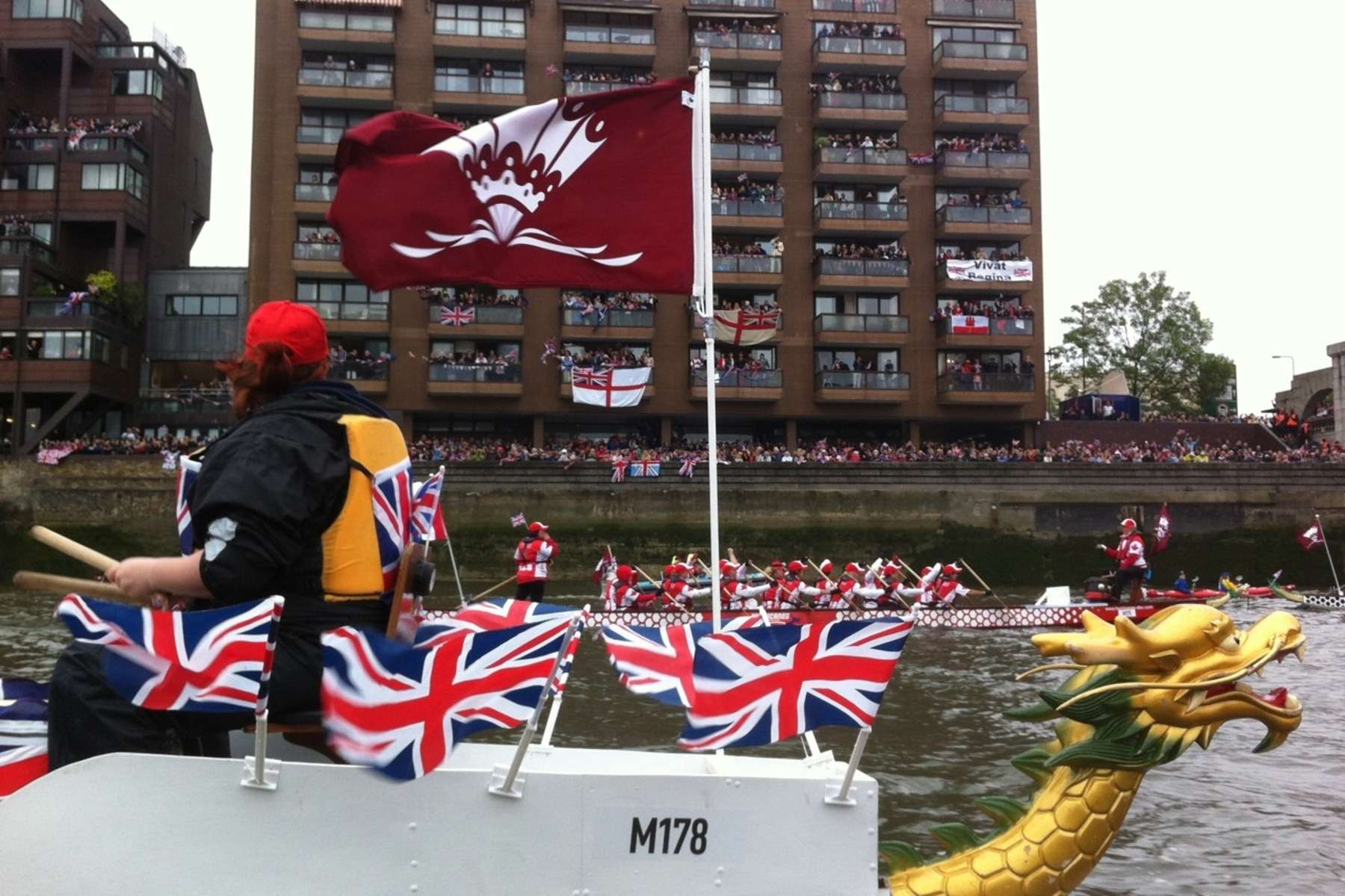 Canada One team paddles the River Thames with thousands of onlookers lining the riverside, cheering from the street and balconies of buildings.