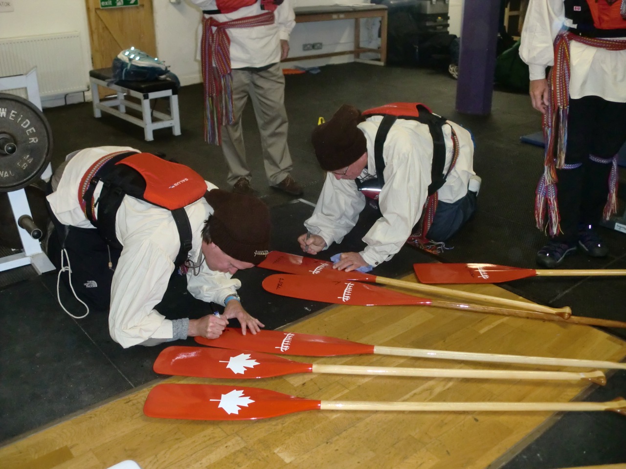 The team signs the Canadian Canoe Museum paddles.