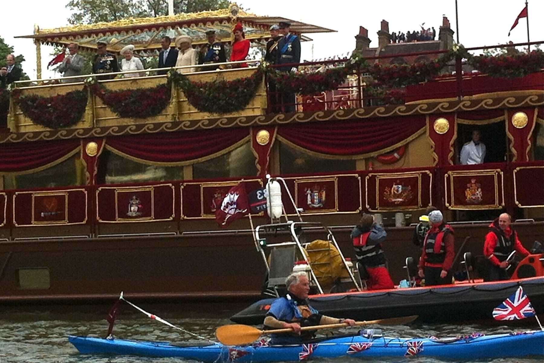 The Queen looks out from the top of a large boat deck alongside other members of the Royal Family.