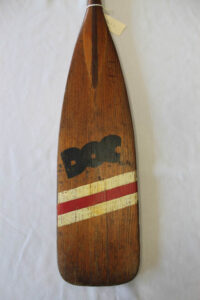 A wooden paddle painted with the name "Doc" and 3 red and white stripes.