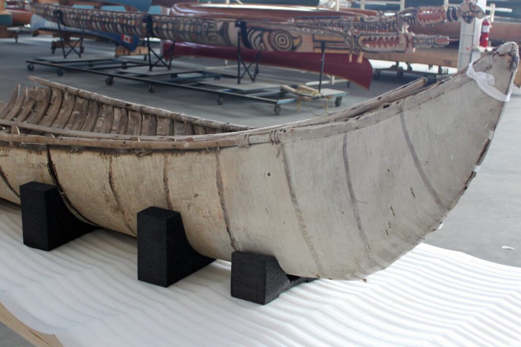 A white birchbark canoe sits sits on black support blocks.