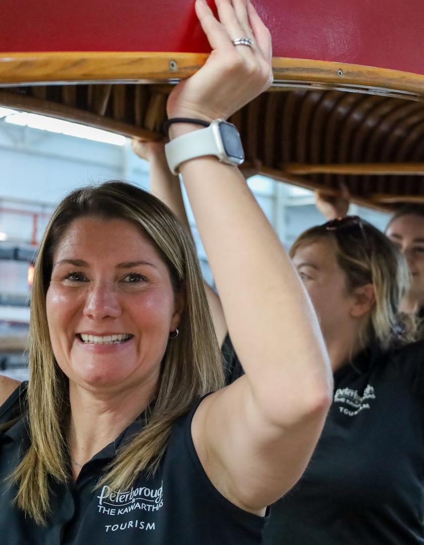 Members of Peterborough and the Kawarthas Tourism team lift (or portage) a red wooden Chestnut canoe to celebrate their sponsorship of The Canadian Canoe Museum's Move the Collection: The Final Portage campaign.