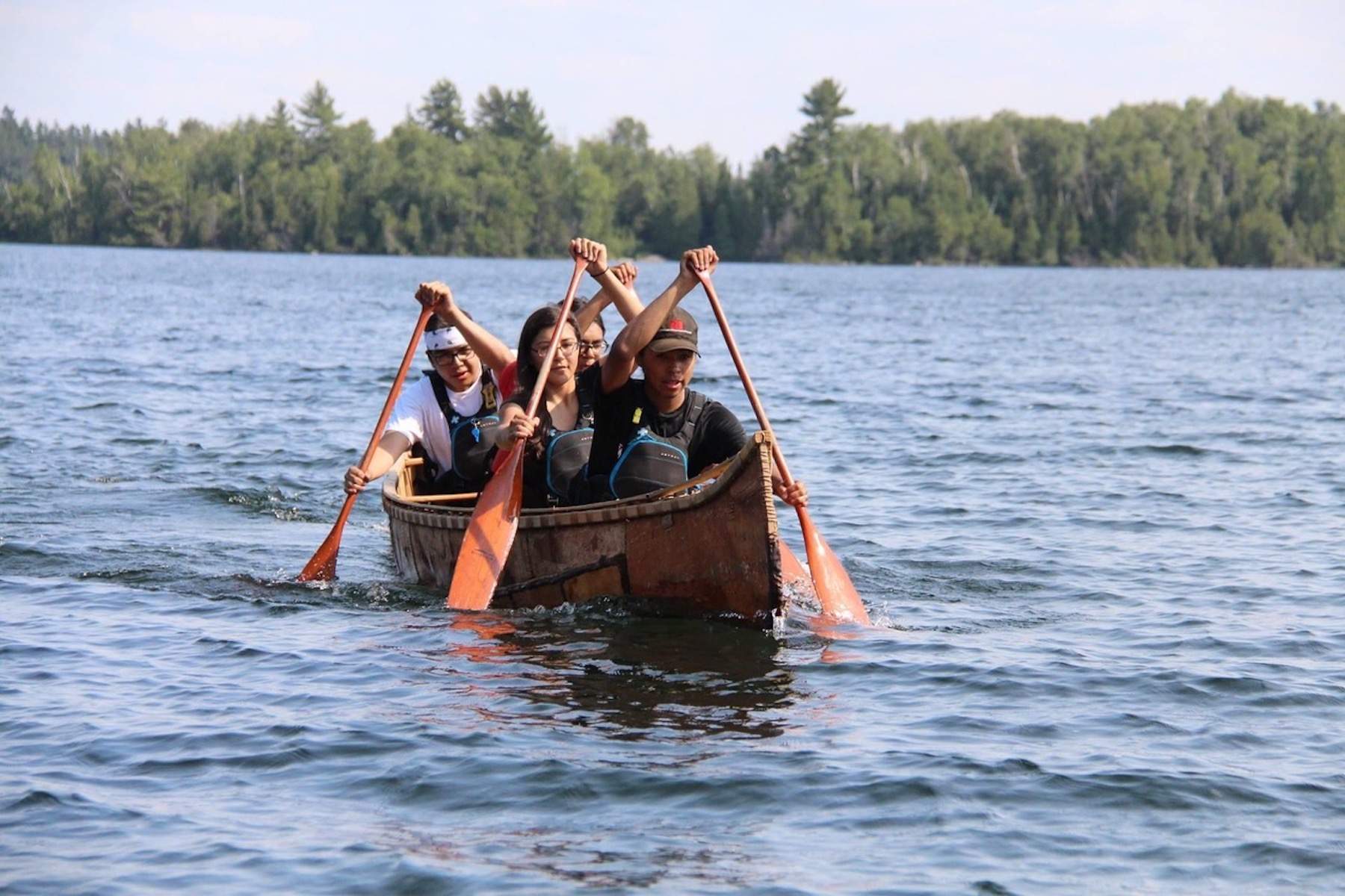 Four Indigenous youth paddle a birch bark canoe.