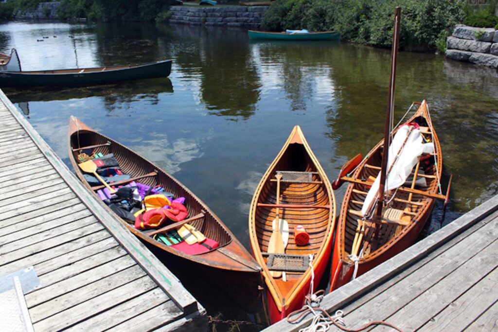 Three canoes tethered to the corner of a dock in calm water.