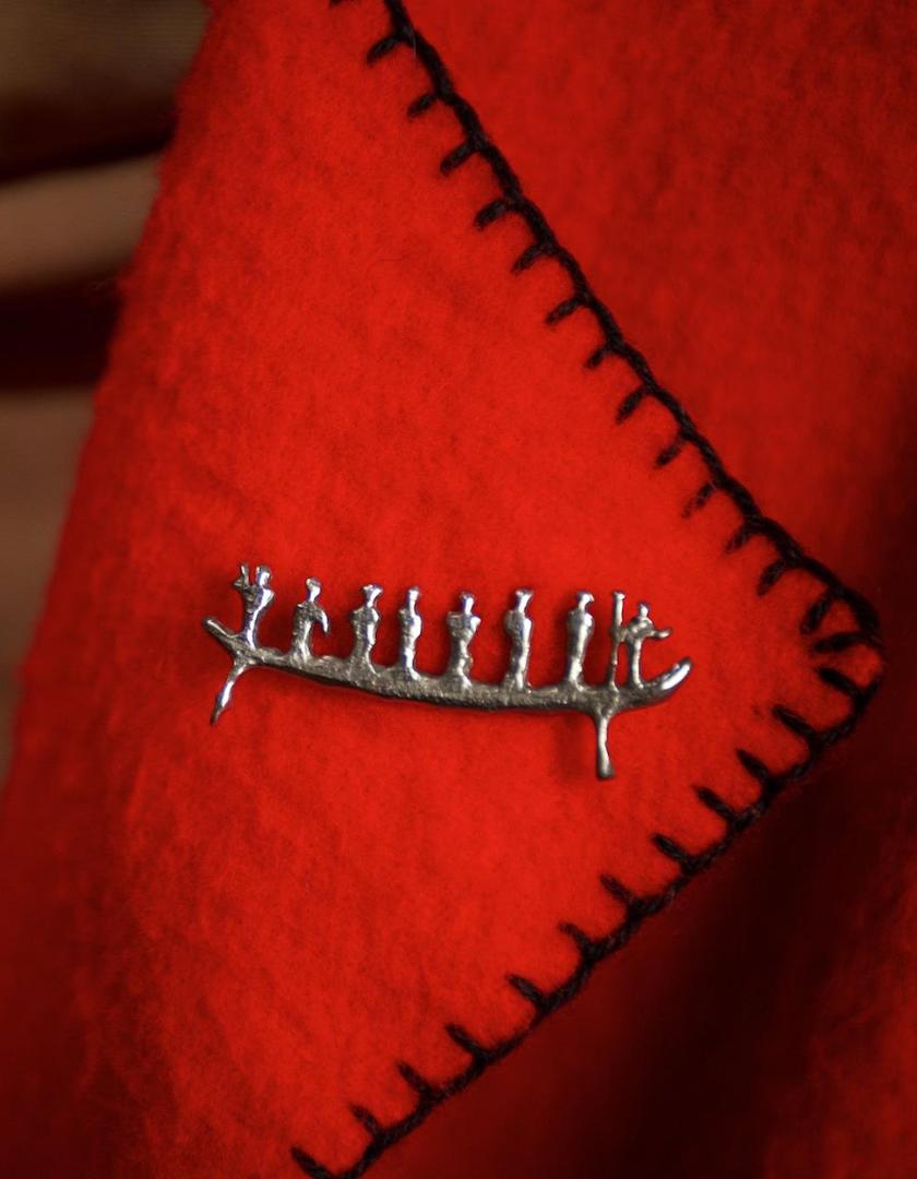 A pewter pin of the pictograph that The Canadian Canoe Museum's logo is inspired by is pinned to the lapel of a red jacket.