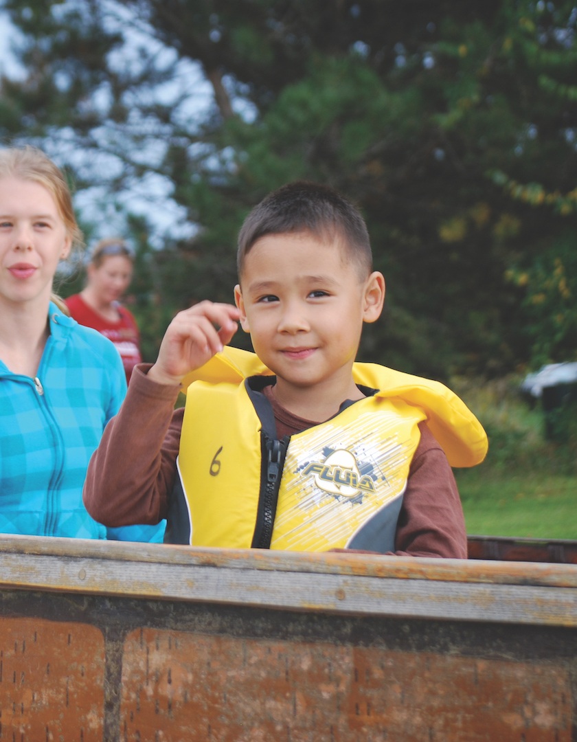 Children stand smiling beside a birch bark canoe outside.