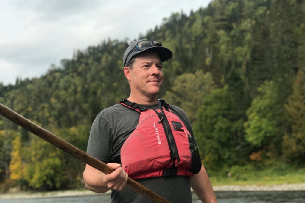 Philip Lee stands outside and holds a canoe paddle.