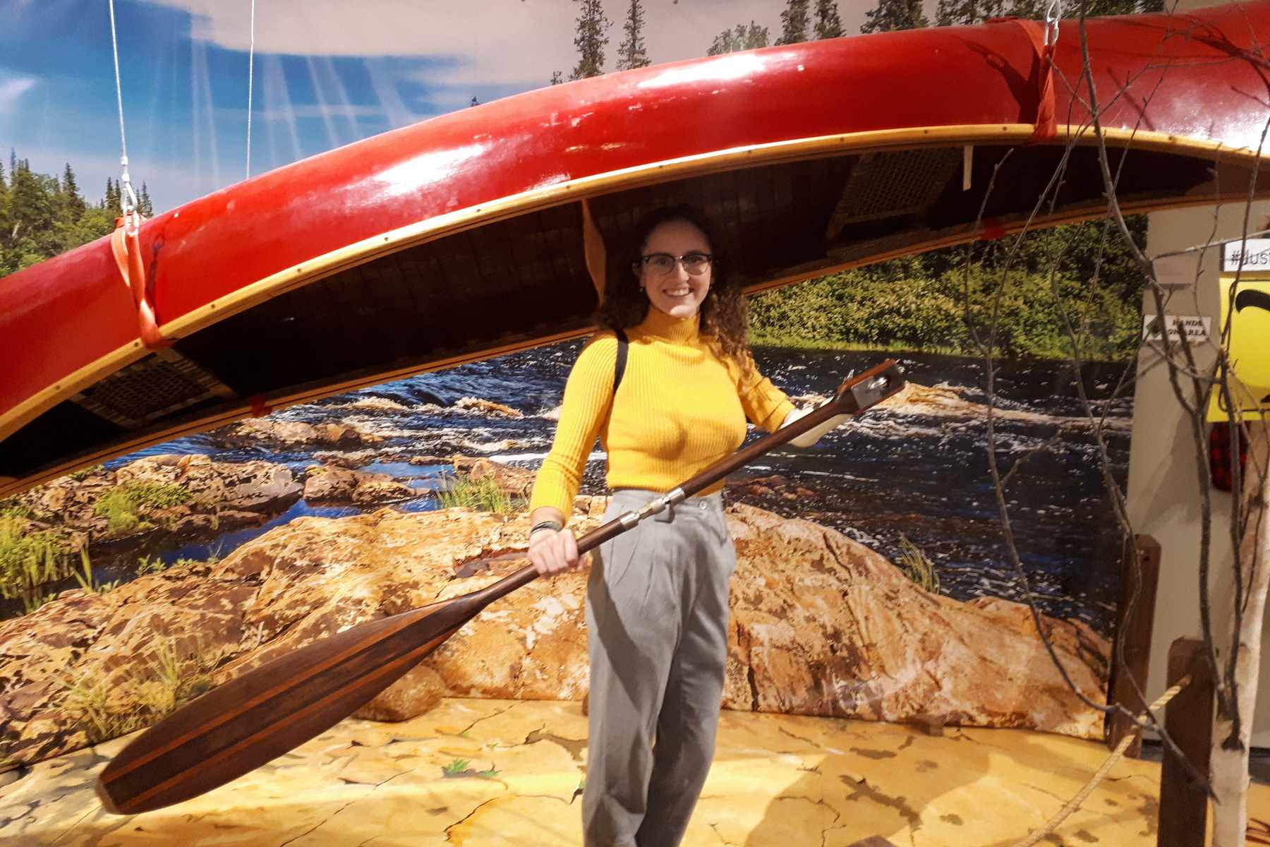 Rachel Quilty posing under a canoe display holding a paddle