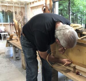 Man leans down to stitch a partially built canoe