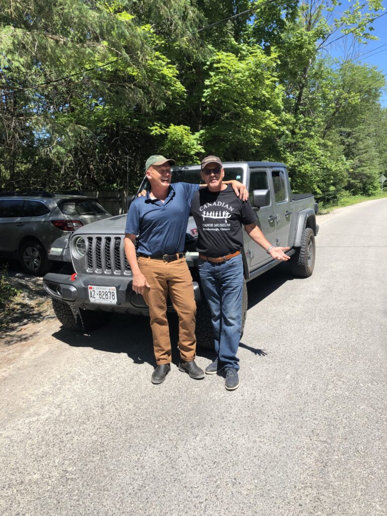 Robin and Jeremy pose in front of a grey Jeep on the side of a tree-lined road in summer