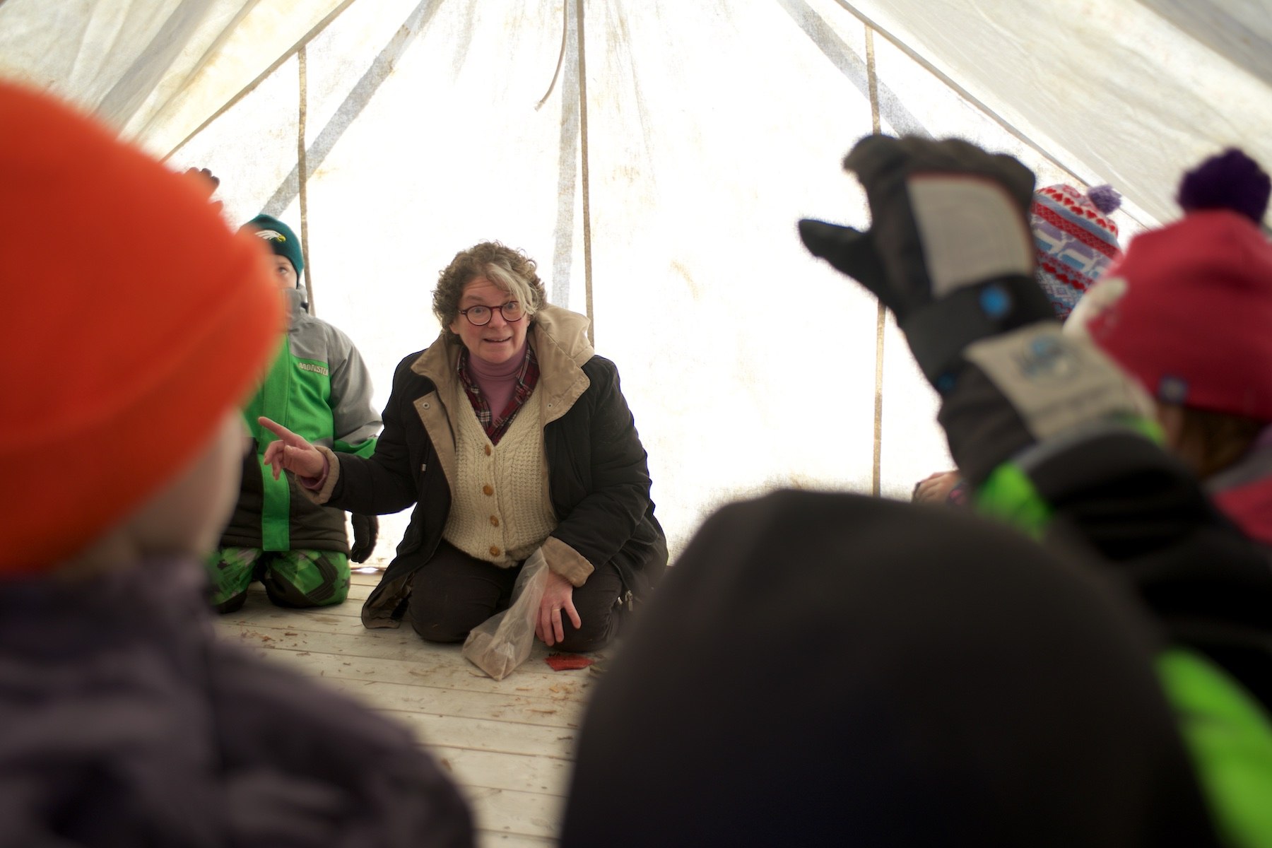 School children sit in a tent as a Canadian Canoe Museum staff member provides instructions. A student raises their hand.