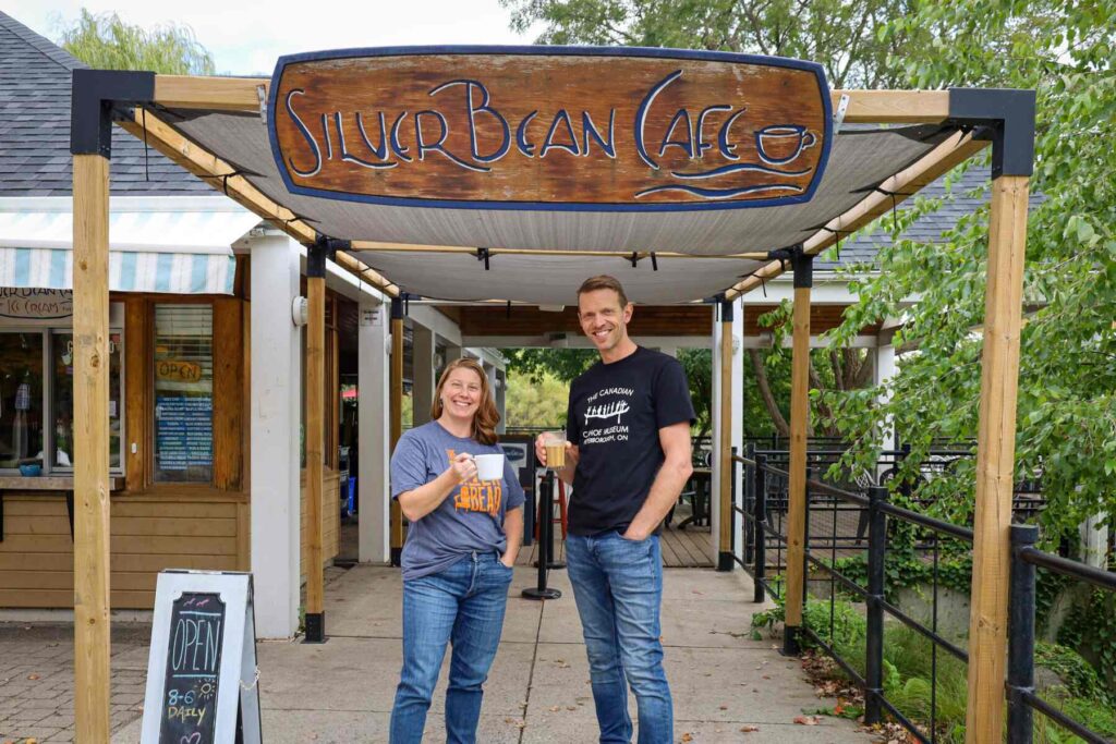 Carolyn Hyslop and Dan Brandsma raising a cup of coffee under the Silver Bean Cafe sign.