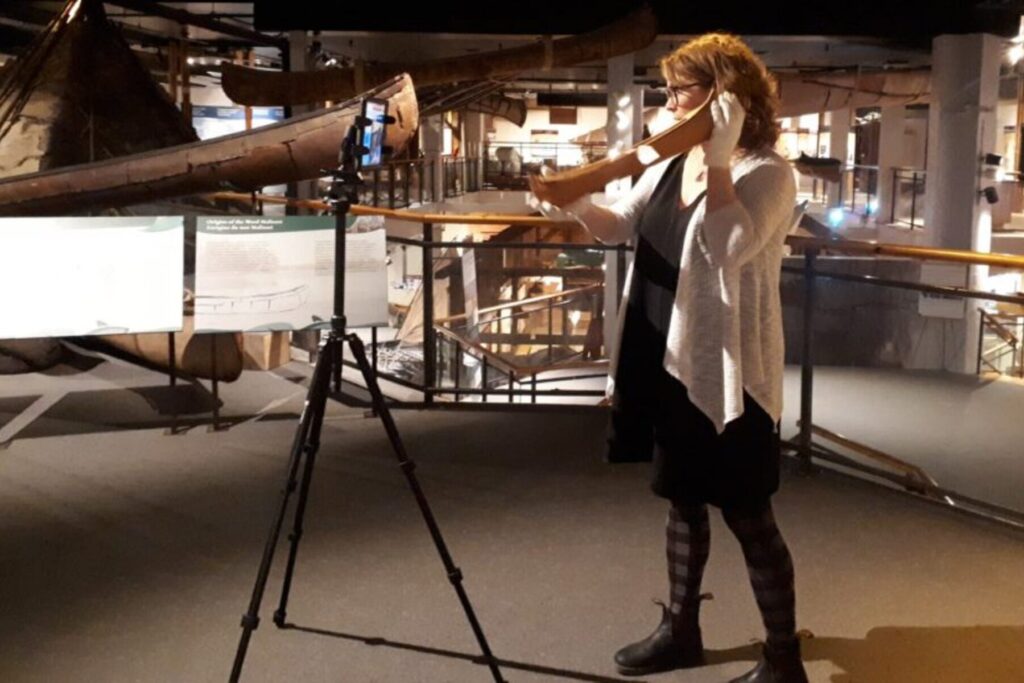 Woman stands in front of a camera and tripod in an exhibit.