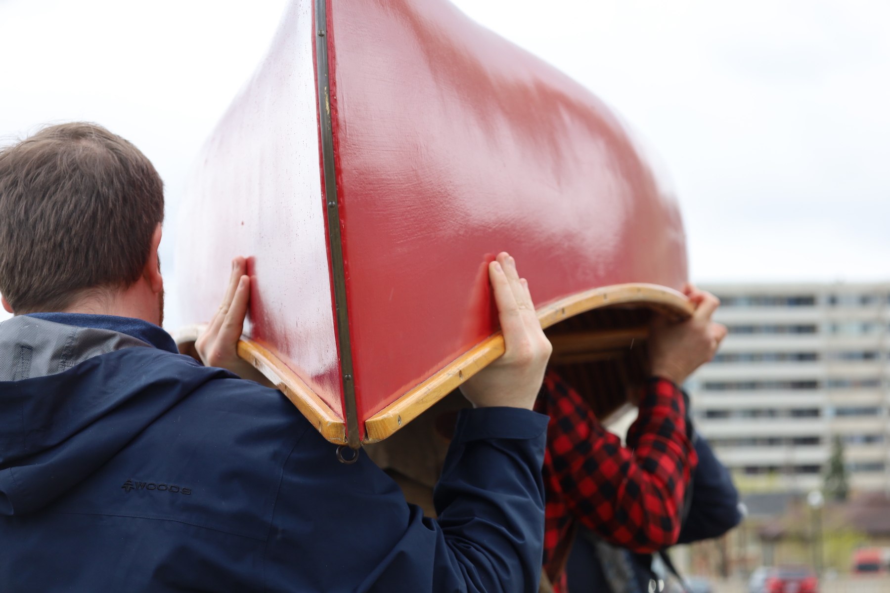 Multiple people carry or portage a red Chestnut canoe through downtown Peterborough, Ontario.