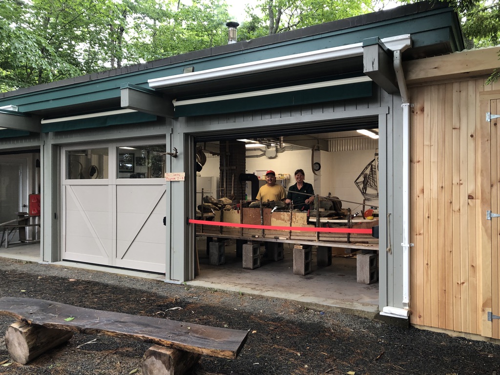 Outdoor shot of a canoe-building workshop with a large grey garage-style doors, one which is open into the workshop