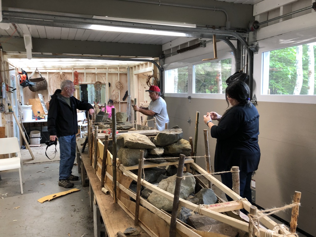 People are helping build a birchbark canoe in a workshop