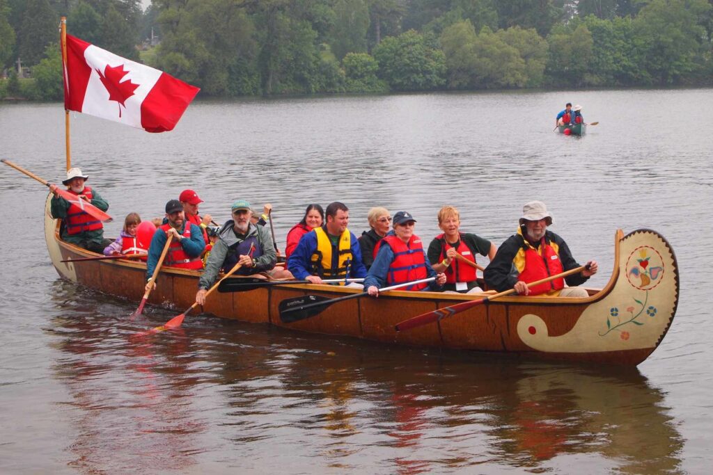 A group of paddlers in a large voyageur canoe with a Canadian flag.