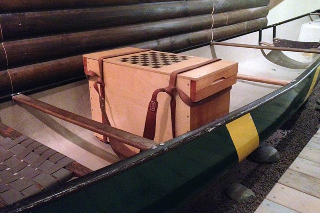 A wooden box, known as a Wanigan, sits in the centre of a green canoe on display