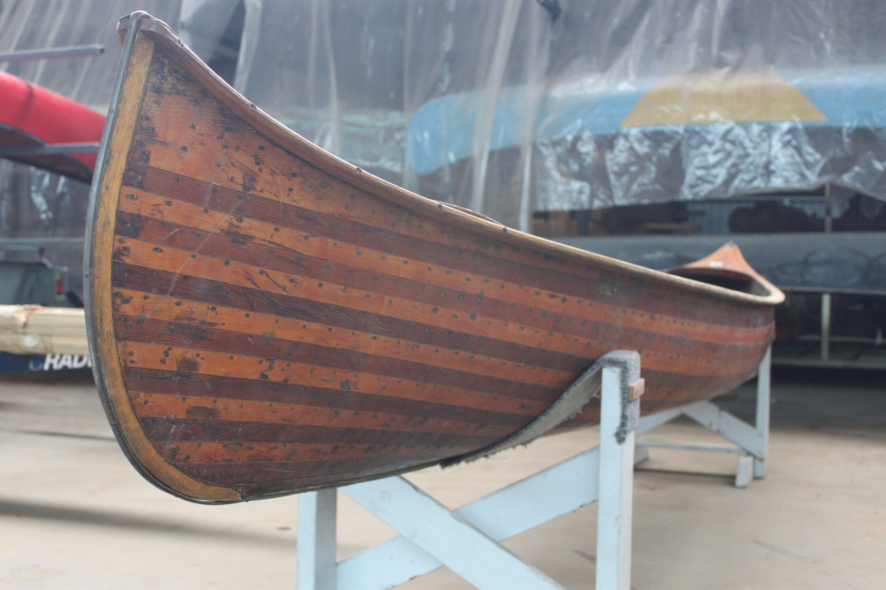 A wooden canoe rests on a metal canoe rack. Image is taken from the perspective of standing at the stern looking toward the bow