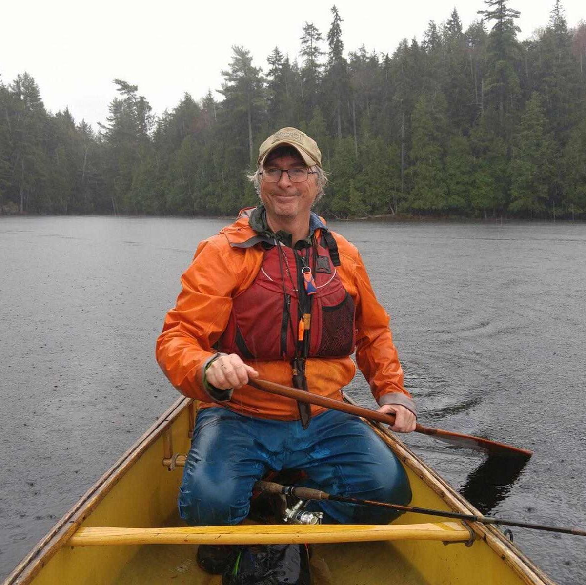 Kevin Callan smiling as he paddles a canoe in a remote lake on a rainy day.