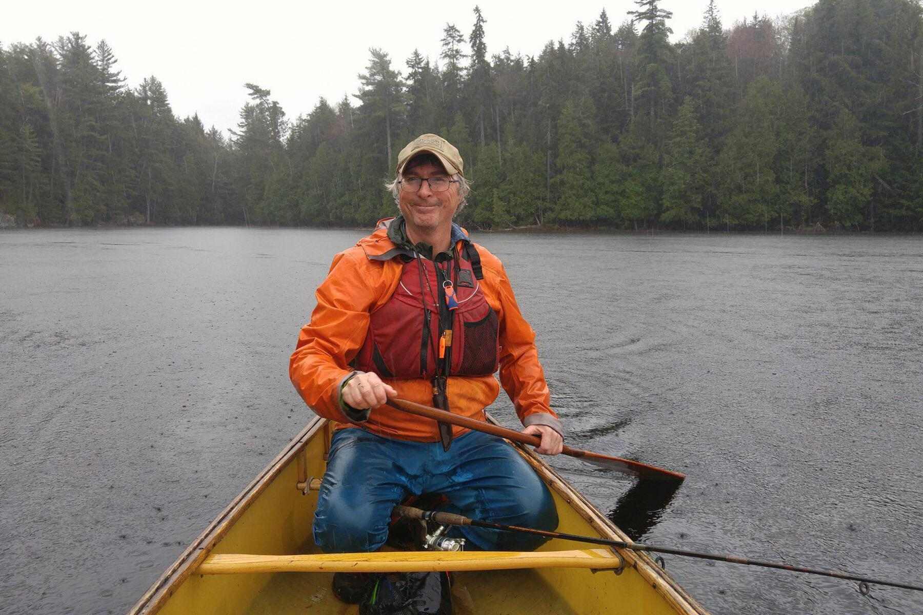Kevin Callan smiling as he paddles a canoe in a remote lake on a rainy day.
