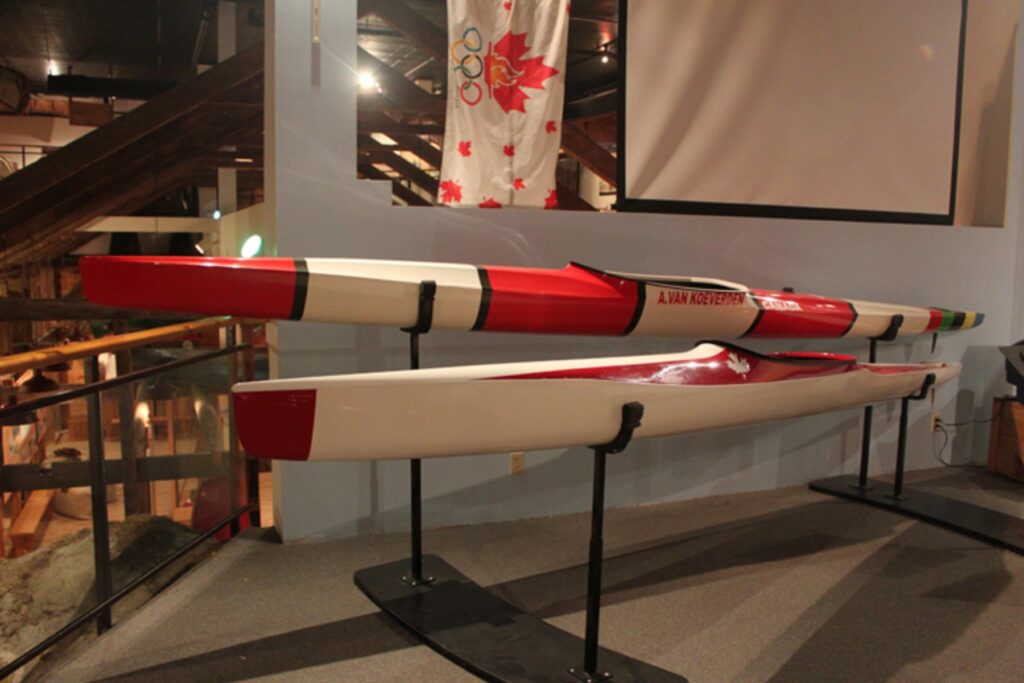 Two olympic kayaks displayed on racks sporting bold red and white colouring and the maple leaf.