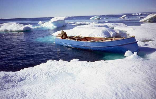 A solo person floats in large blue canoe surrounded by floating ice