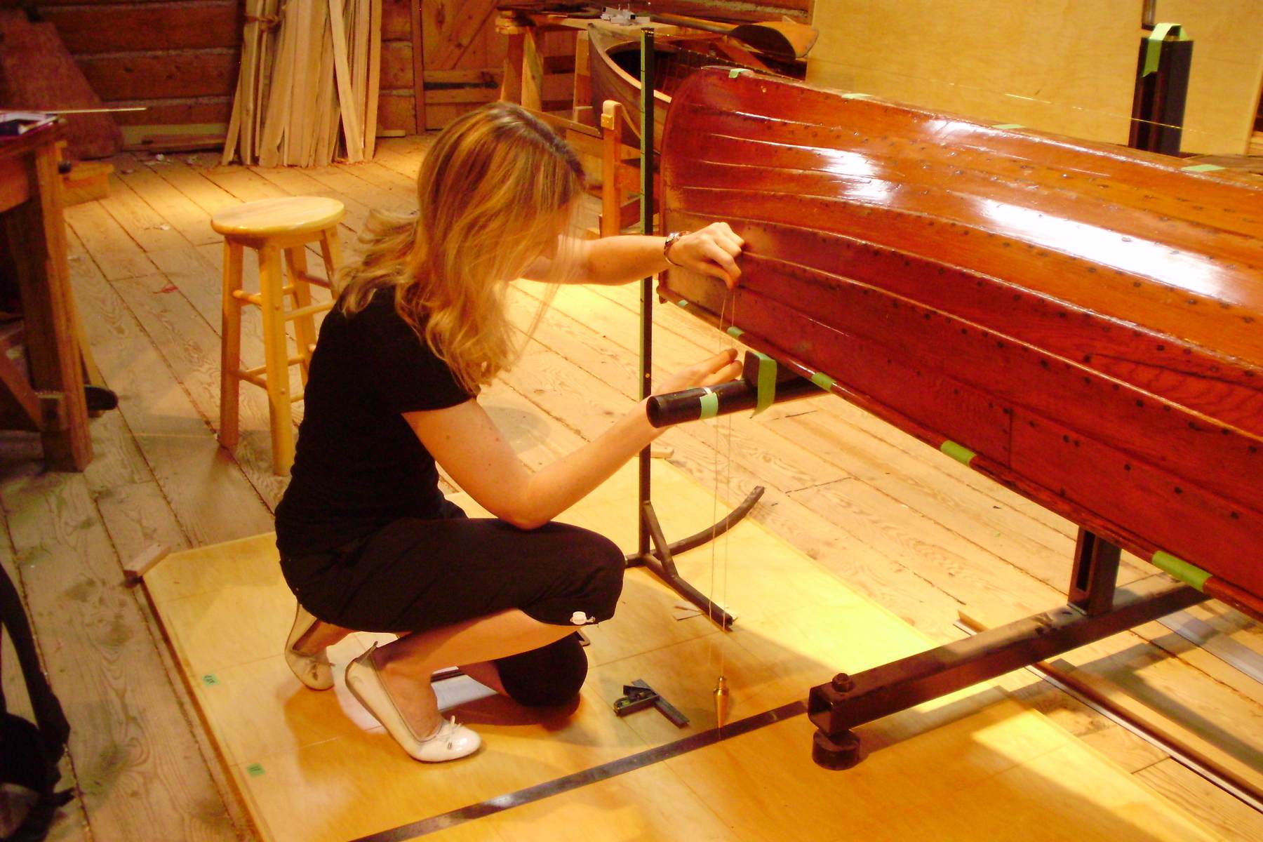 A lapstrake canoe canoe sits upside down while someone measures and tapes parts of its gunwales.