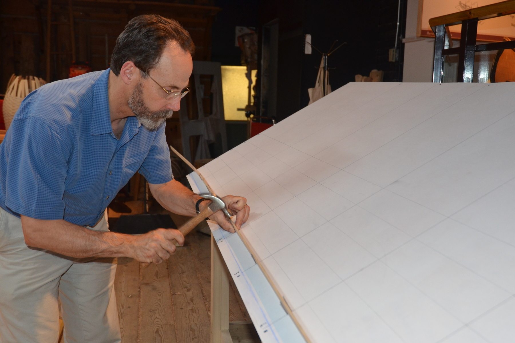 A man carefully hammers nails on a workshop table to secure a small strip of wood.