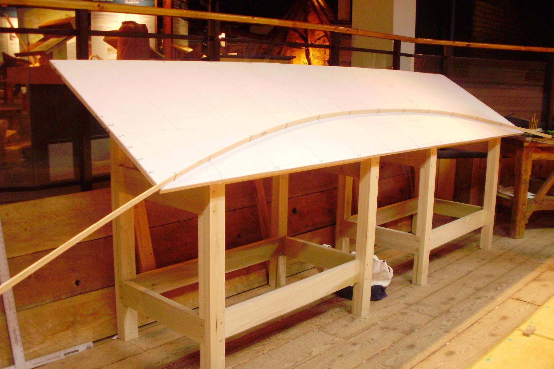 A large workshop table holds a single strip of wood