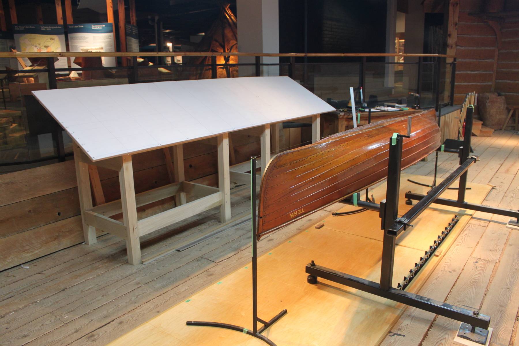 A wooden lapstrake canoe canoe sits upside down on black support bars