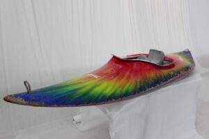 Multicolour tie-dyed kayak sits on display with a white backdrop.