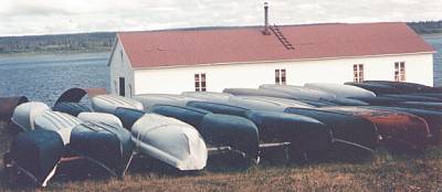 Several canoes stored on racks outside a white building beside water