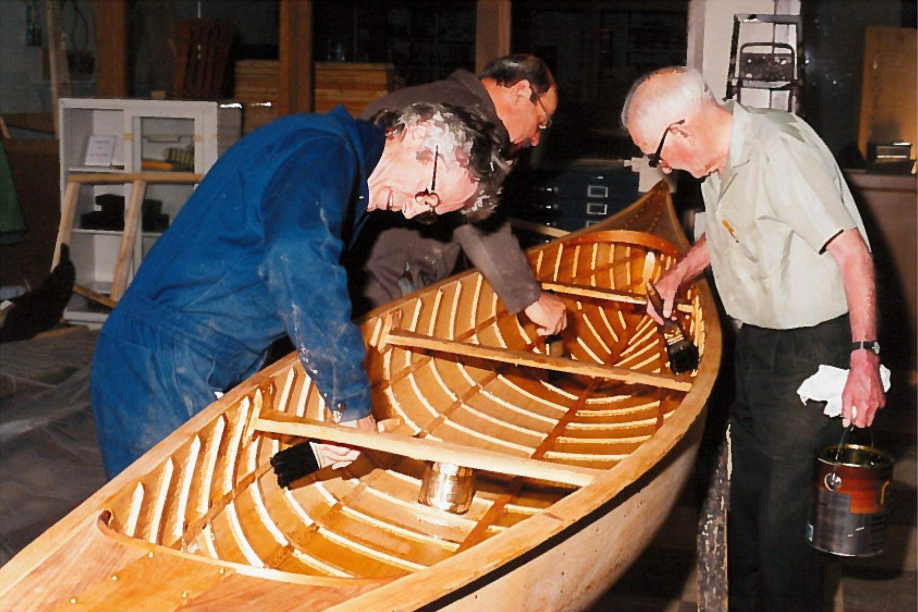 Three men are working on finishing touches to the inside of a canoe.